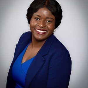 Headhot of Amie - a black woman, smiling, and who is wearing a blue blazer and blue blouse.