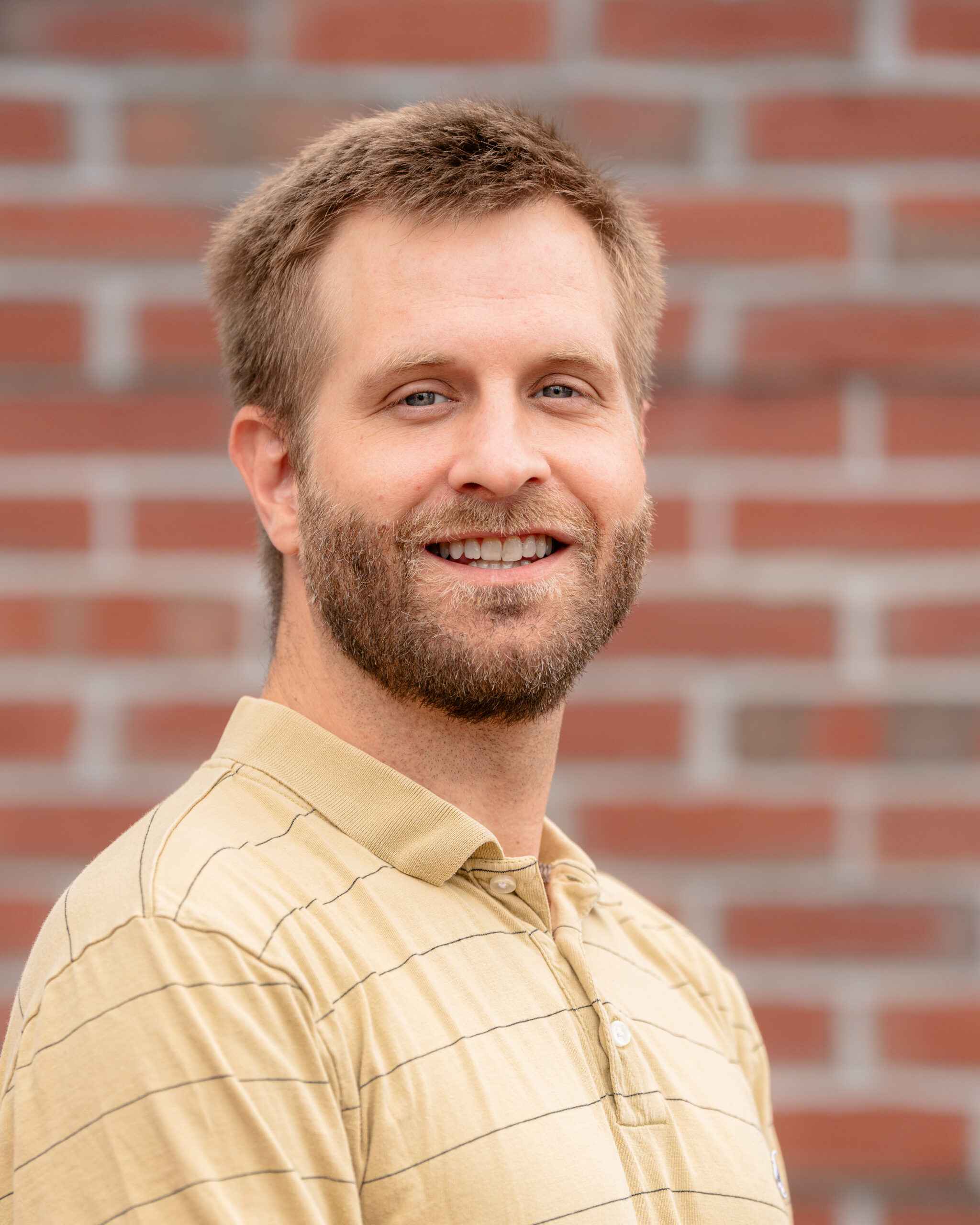 Caleb, a white man with blue eyes, short blond hair, a beard and a green shirt smiles.