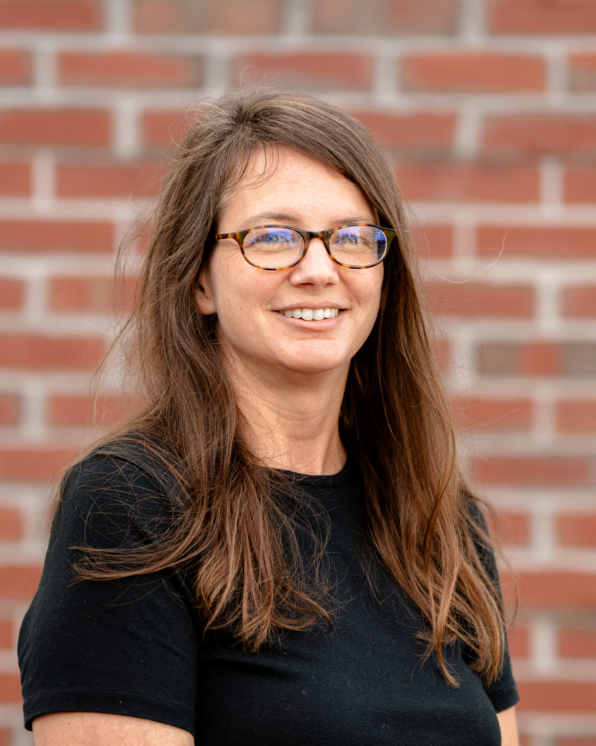 Carly, a white woman with brown hair, glasses, and a black shirt.