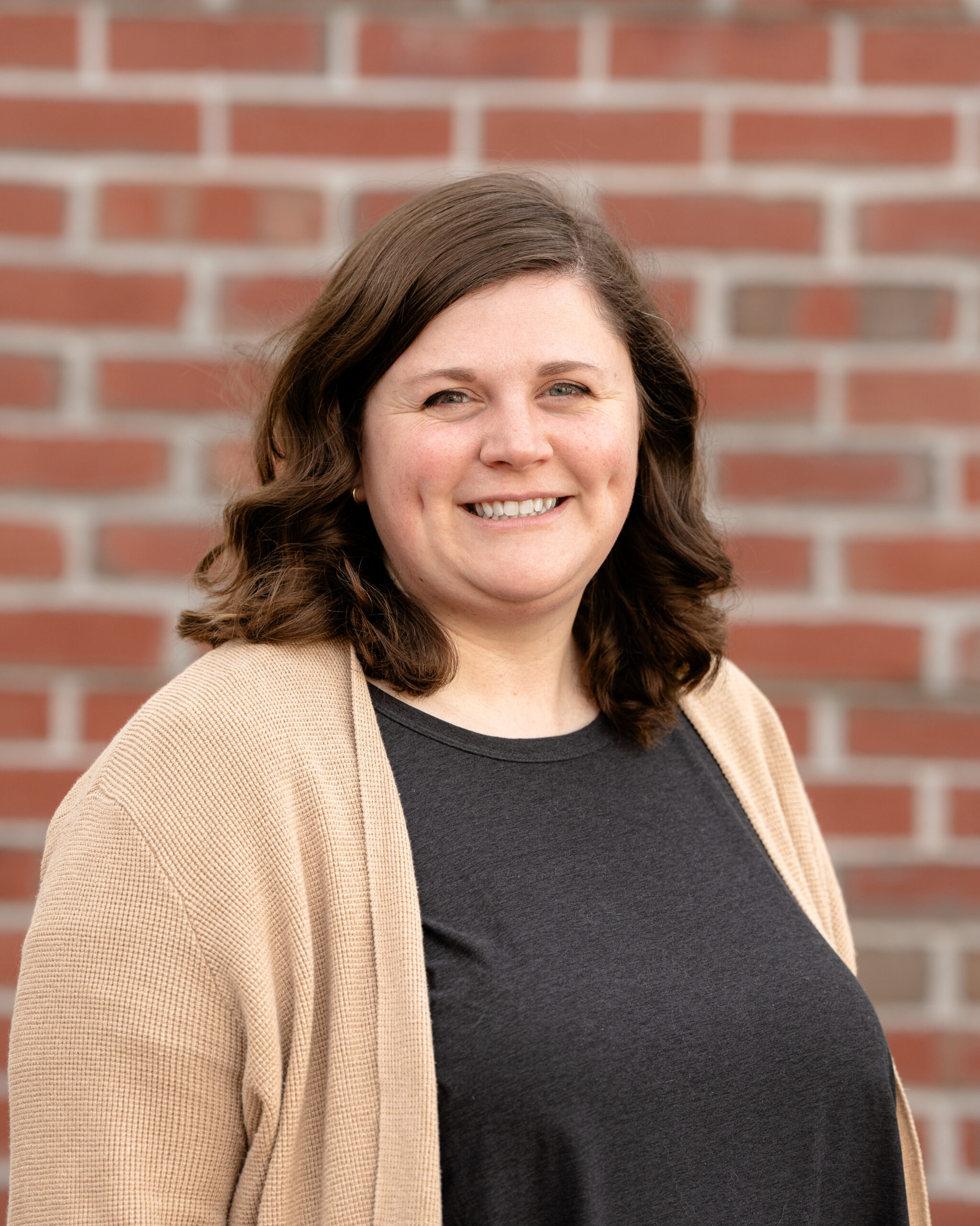 Casey is a white woman with curly brown hair. She is wearing a black shirt with a khaki-colored cardigan.