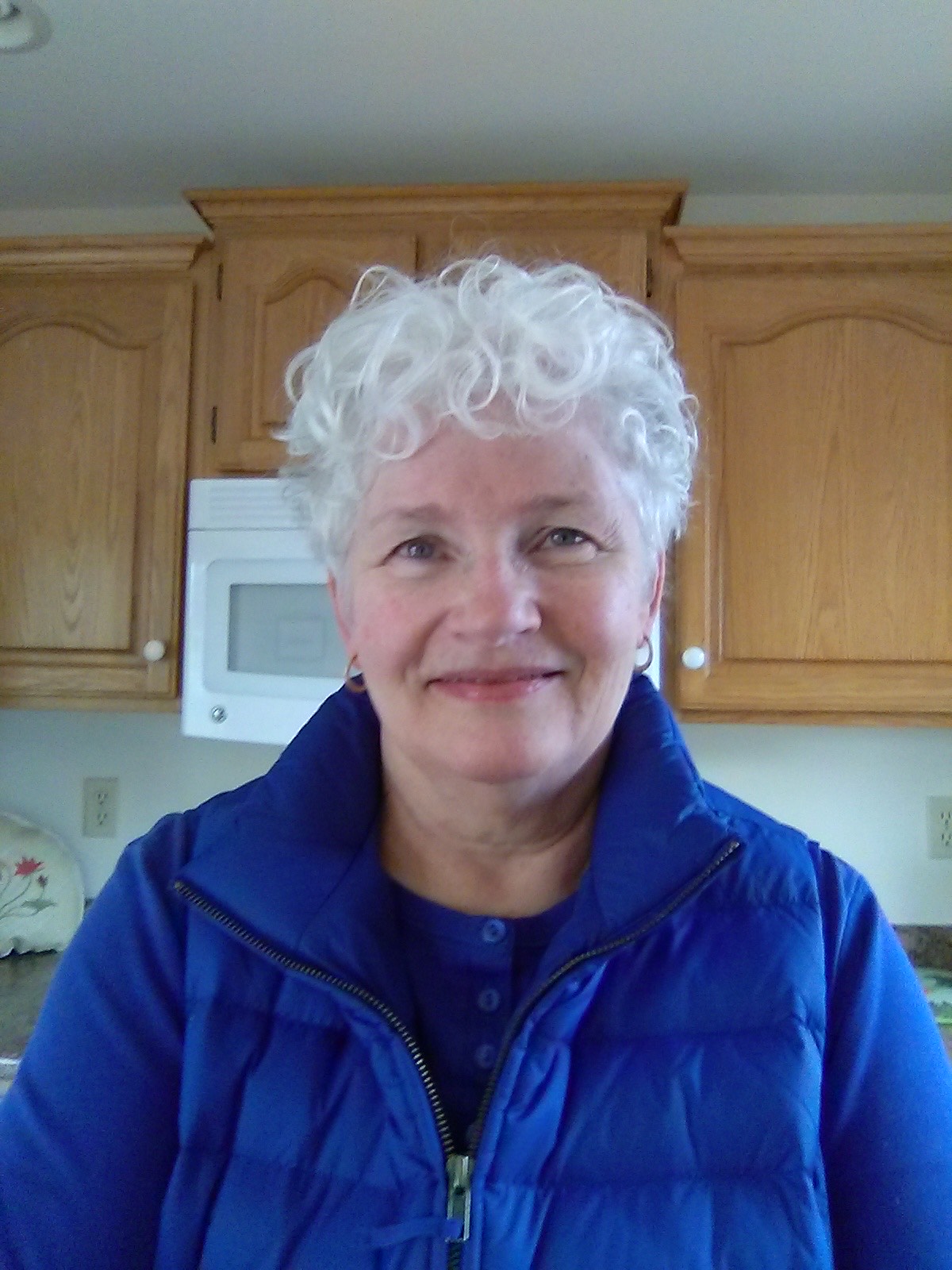 LuAnne, a white woman with short white hair, stands in a kitchen. She wears a blue jacket.