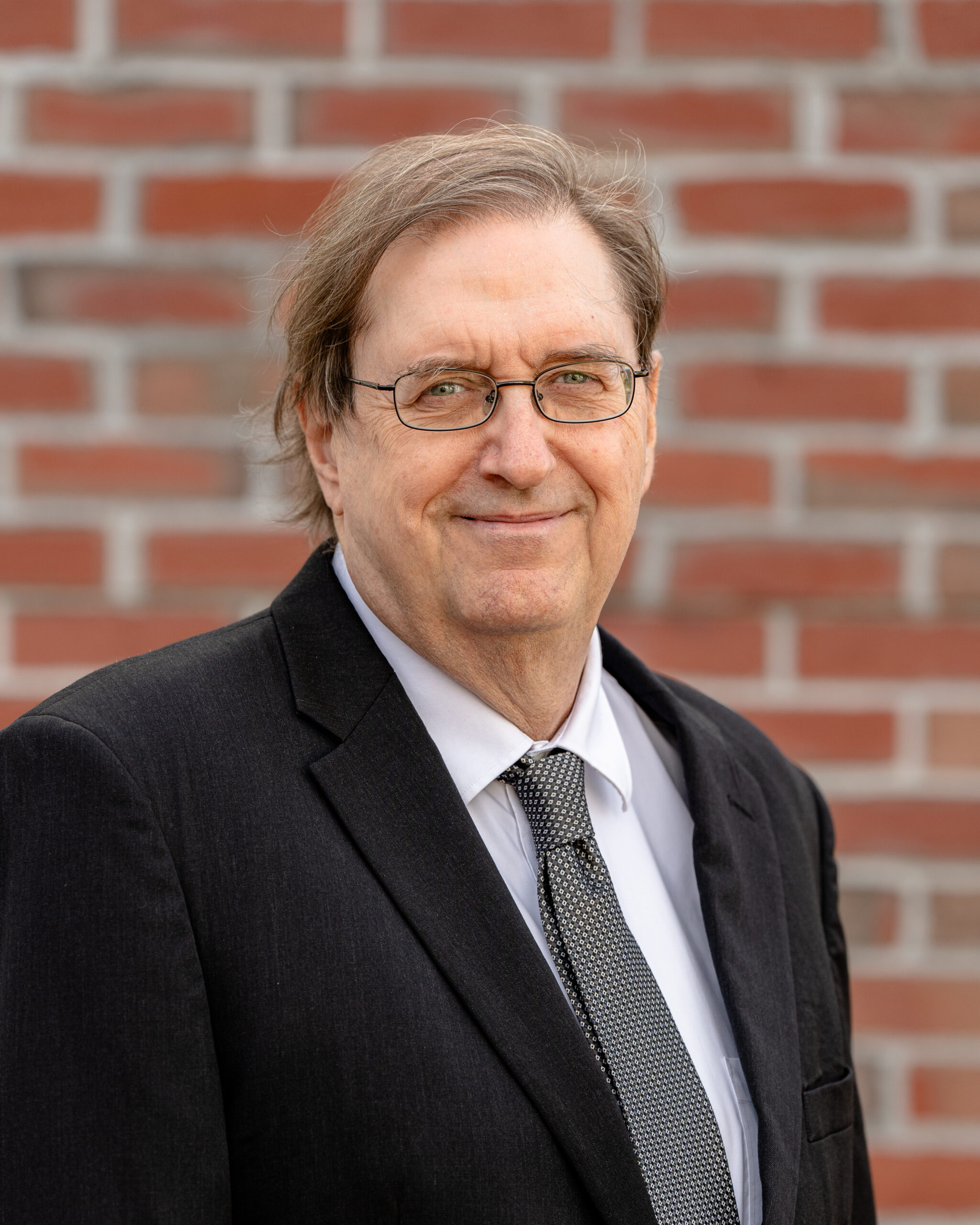 Mark a white man with brown hair and glasses. He wears a black blazer.