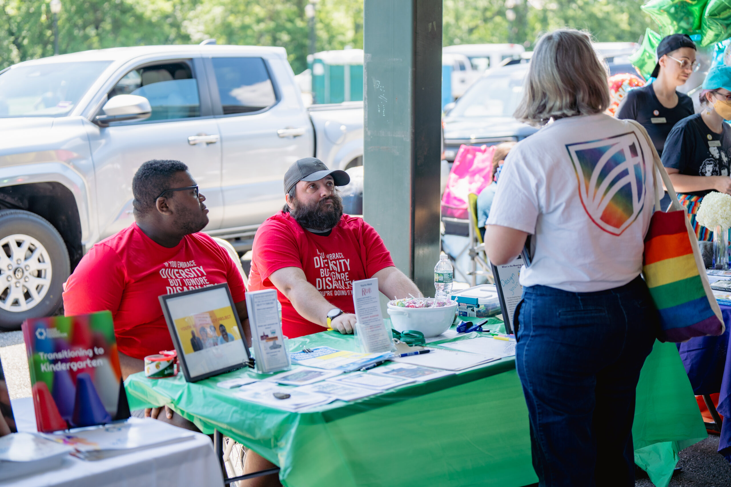 Two DRM staffers sit at a table and speak to someone at Disability Pride 2024.