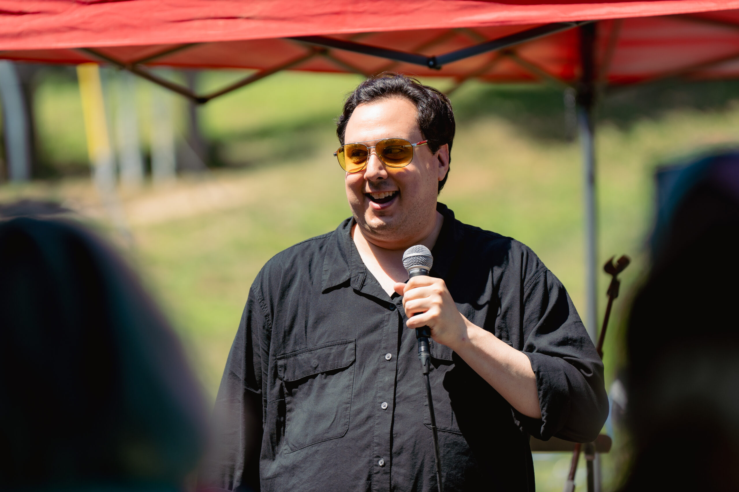 Man wearing a black shirt and yellow sunglasses holding a microphone.