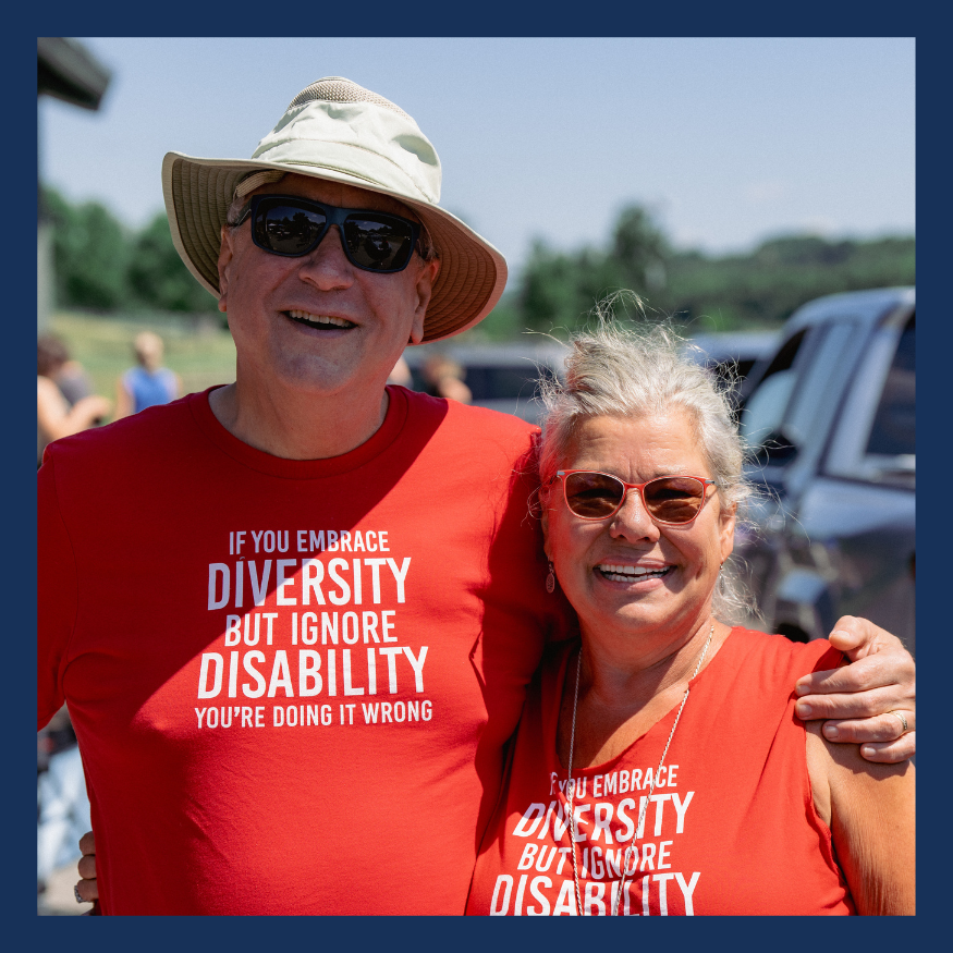 Andy Sarapas and Kim Moody stand next to each other in matching red shirts that read if you embrace diversity and forget disability you are doing it wrong.