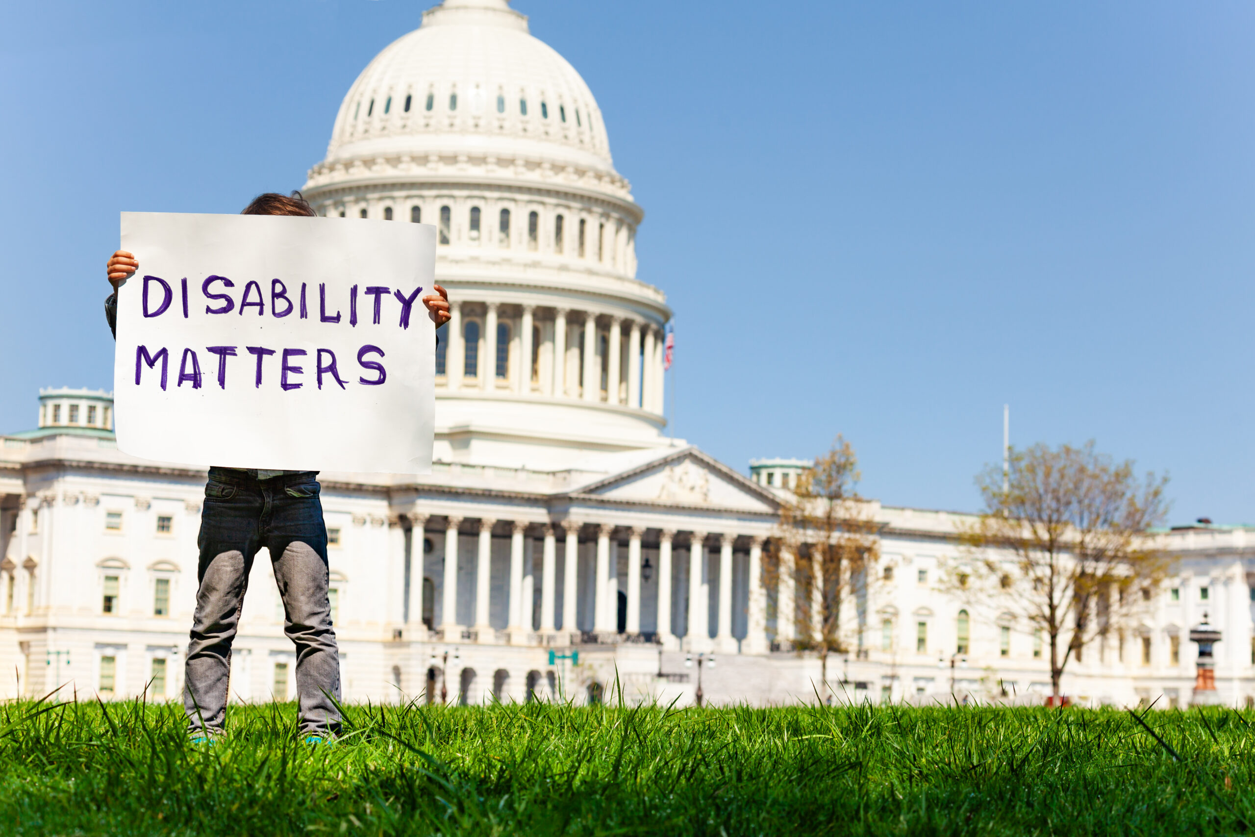 A sign that reads Disability Matters is held up in front of the Capitol Building.