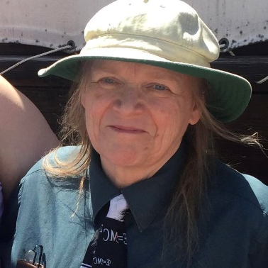 Vickie, a white woman with shoulder length gray hair, wears a rimmed hat and a green shirt.