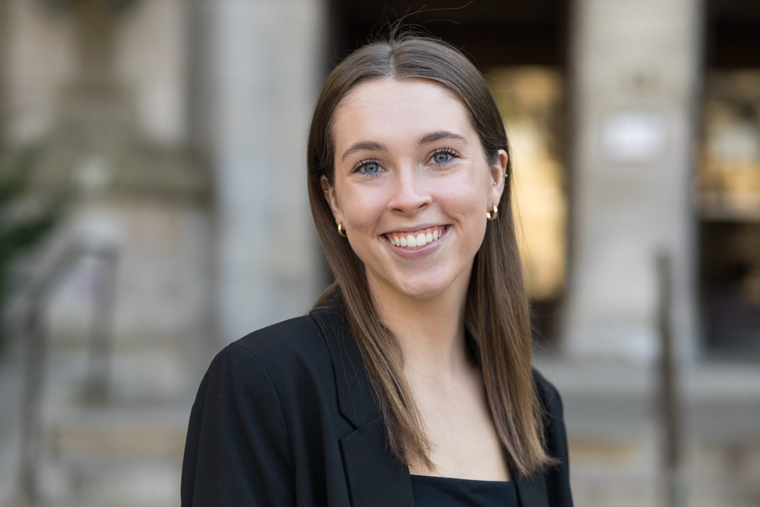 Tess, a white woman with medium length brown hair. She wears a black top and a black blazer.