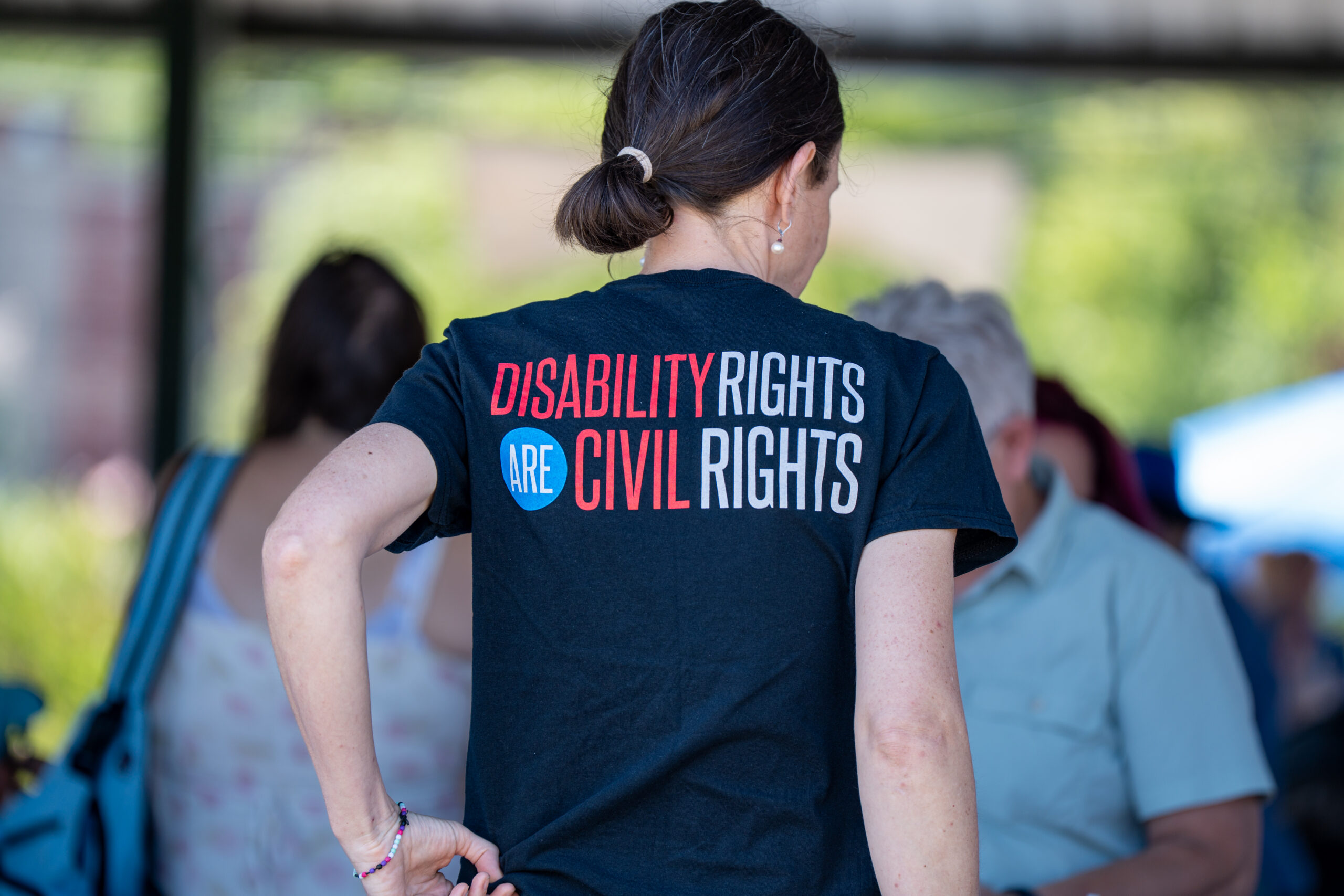 Photo of a person from behind at Disability Pride. Their shirt reads "Disability rights are civil rights"